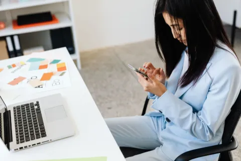 Seseorang sedang menggunakan smartphone produktivitas kerja untuk memeriksa dokumen kantor di meja kerja