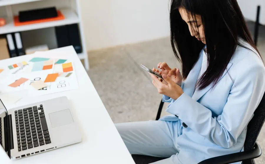 Seseorang sedang menggunakan smartphone produktivitas kerja untuk memeriksa dokumen kantor di meja kerja