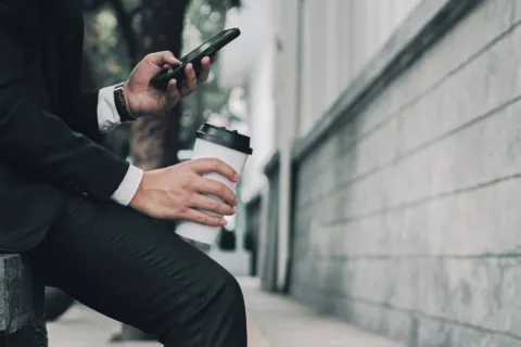 Seseorang menggunakan smartphone untuk kerja sambil memeriksa dokumen dan aplikasi kantor