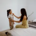 Anak kecil sedang belajar memakai sepatu sendiri di ruang tamu sebagai bentuk cara mendukung kemandirian anak