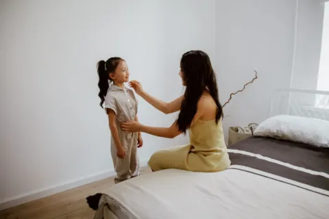 Anak kecil sedang belajar memakai sepatu sendiri di ruang tamu sebagai bentuk cara mendukung kemandirian anak