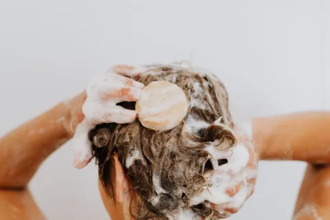 Seseorang sedang mencuci rambut di kamar mandi sebagai cara mengatasi kulit kepala berminyak yang lepek
