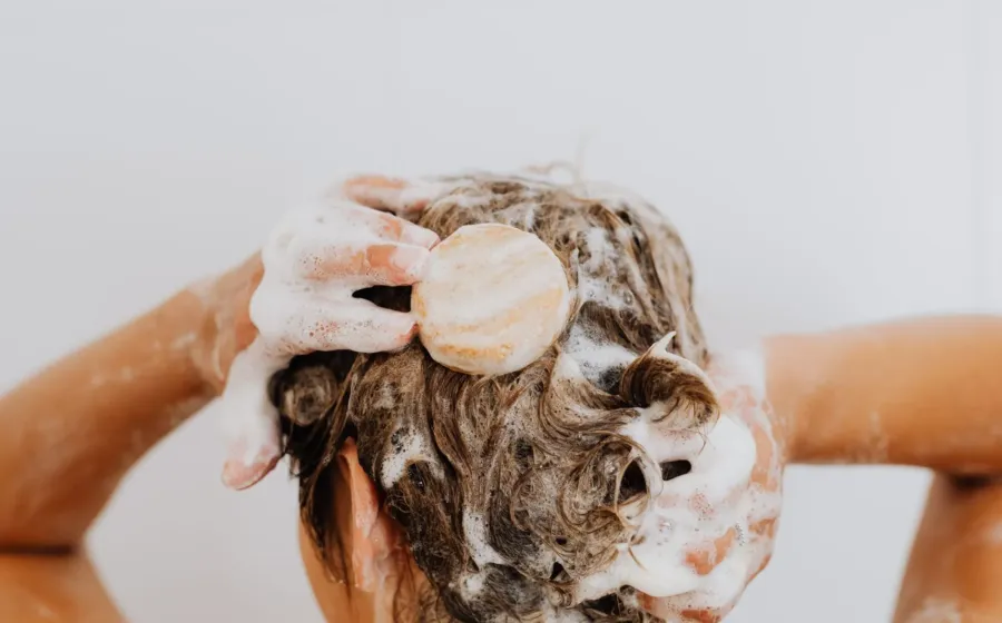 Seseorang sedang mencuci rambut di kamar mandi sebagai cara mengatasi kulit kepala berminyak yang lepek