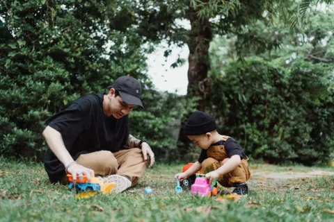 Ayah dan anak balita sedang asyik bermain miniatur mobil di lantai rumah untuk mengenal transportasi