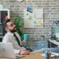 Pekerja kantor tersenyum santai menikmati kopi di meja kerja yang rapi untuk gaya hidup seimbang