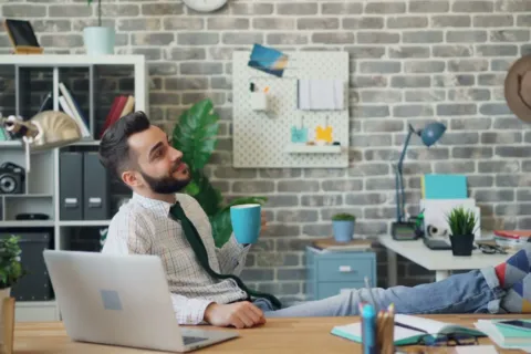 Pekerja kantor tersenyum santai menikmati kopi di meja kerja yang rapi untuk gaya hidup seimbang