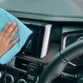 Seseorang sedang mengusap dashboard mobil menggunakan kain mikrofiber bersih untuk perawatan interior