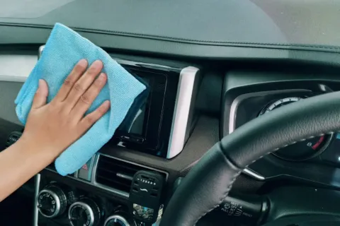 Seseorang sedang mengusap dashboard mobil menggunakan kain mikrofiber bersih untuk perawatan interior