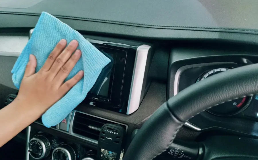 Seseorang sedang mengusap dashboard mobil menggunakan kain mikrofiber bersih untuk perawatan interior